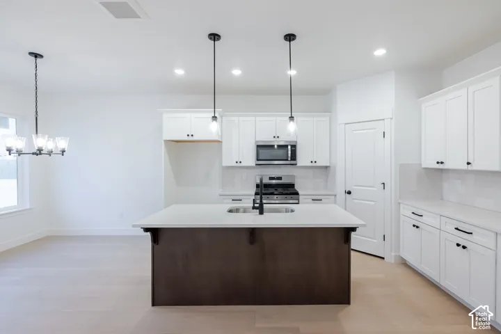Kitchen featuring a central island, stainless steel appliances, white cabinetry with black hardware, white subway tile backsplash, and light wood-finish flooring