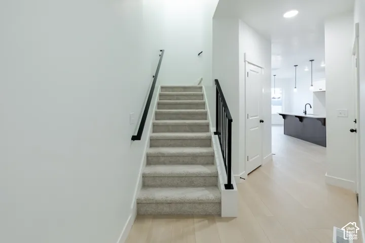 Carpeted staircase with black metal balusters, light wood-finish flooring, white paneled doors, and contemporary pendant lighting