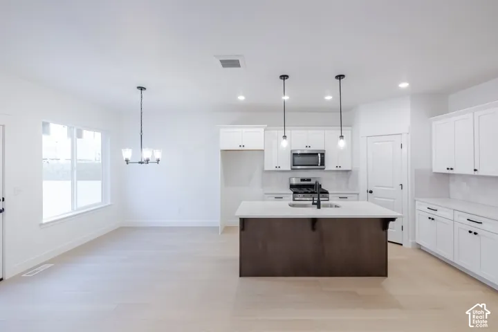 Bright open-concept kitchen featuring white shaker cabinetry, stainless steel appliances, a dark wood-finish island with a sink, and pendant lighting