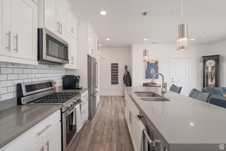 Kitchen featuring appliances with stainless steel finishes, quartz counter tops, white cabinets, a kitchen island with sink, hanging light fixtures, and recessed lighting