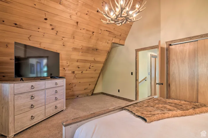 Carpeted bedroom with vaulted ceiling, a chandelier, and a closet