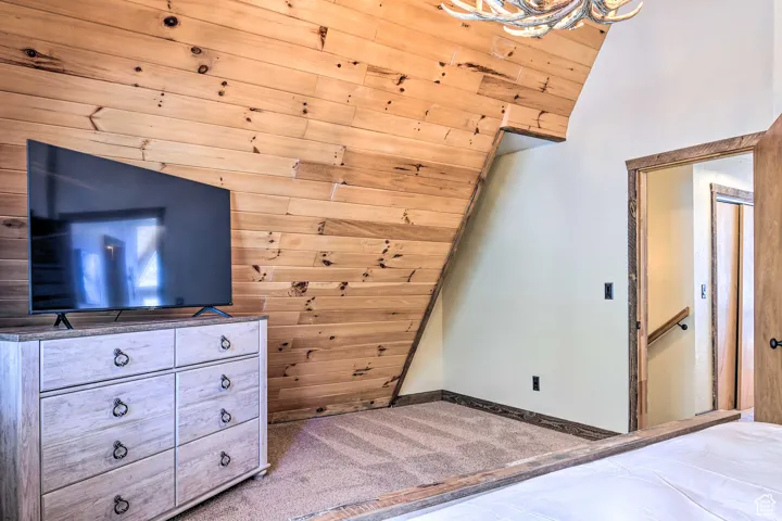 Carpeted bedroom featuring wood walls and vaulted ceiling