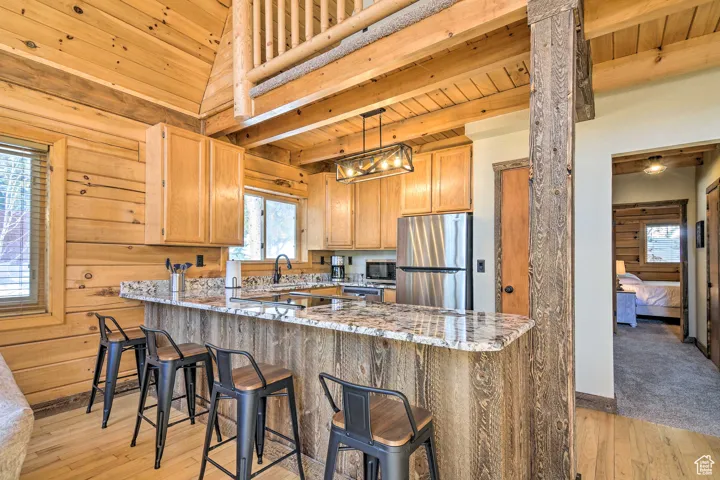 Kitchen with a wood ceiling with exposed beams, light wood-style flooring, decorative light fixtures, light stone counters, and stainless steel appliances