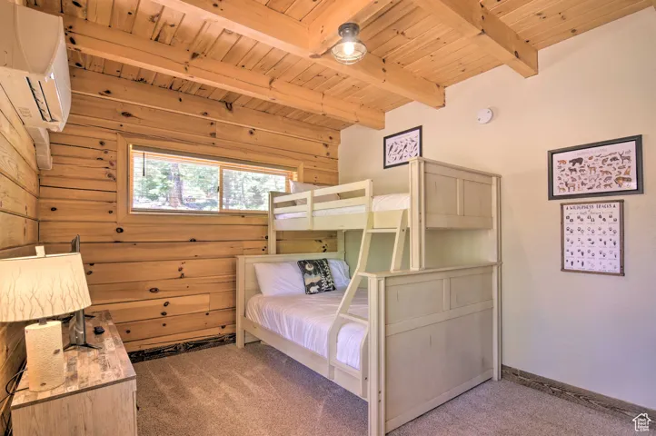 Carpeted bedroom with a wood ceiling with exposed beams and a wall mounted air conditioner
