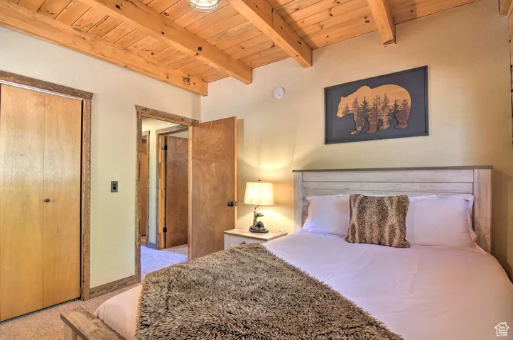 Bedroom with a wooden ceiling with exposed beams, a closet, and light colored carpet