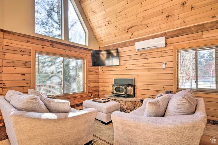 Living room with a wood stove, wooden walls, wood finished floors, wooden ceiling, and high vaulted ceiling