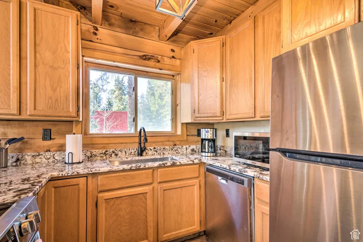 Kitchen featuring stainless steel appliances, a wooden ceiling with exposed beams, light stone countertops, and brown cabinetry