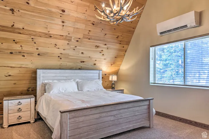 Bedroom featuring wooden walls, a wall mounted AC, carpet, a chandelier, and vaulted ceiling
