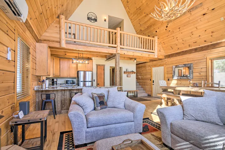Living area with wooden walls, a chandelier, light wood-type flooring, high vaulted ceiling, and wood ceiling