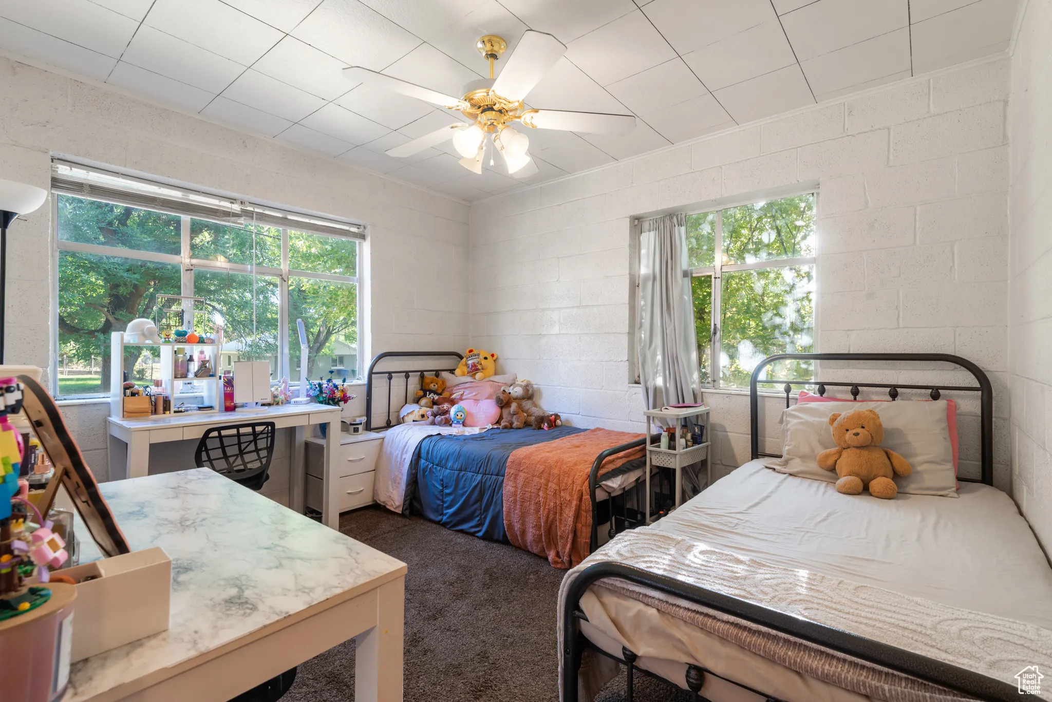 Bedroom with concrete block wall, ceiling fan, and dark colored carpet