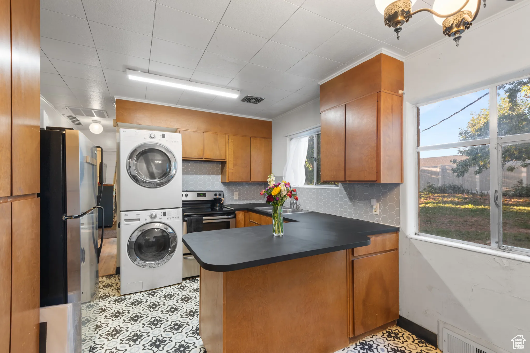 Kitchen featuring brown cabinetry, a peninsula, stainless steel appliances, tasteful backsplash, and dark countertops