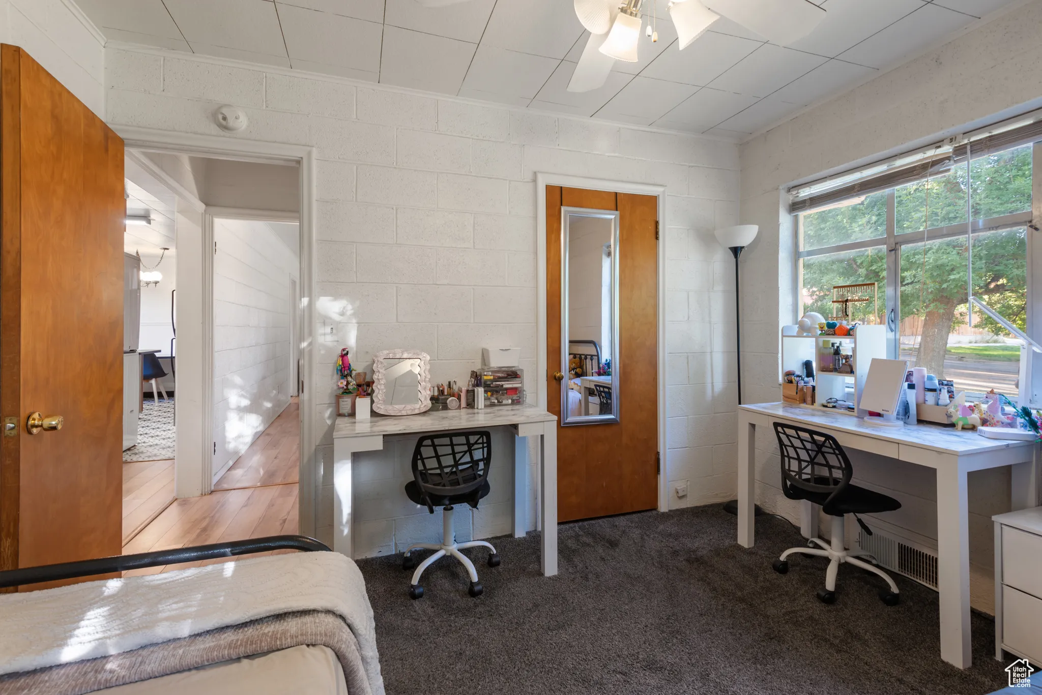 Carpeted bedroom with a desk, a ceiling fan, and concrete block wall