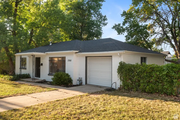 Ranch-style house with concrete block siding, a shingled roof, a front lawn, and an attached garage