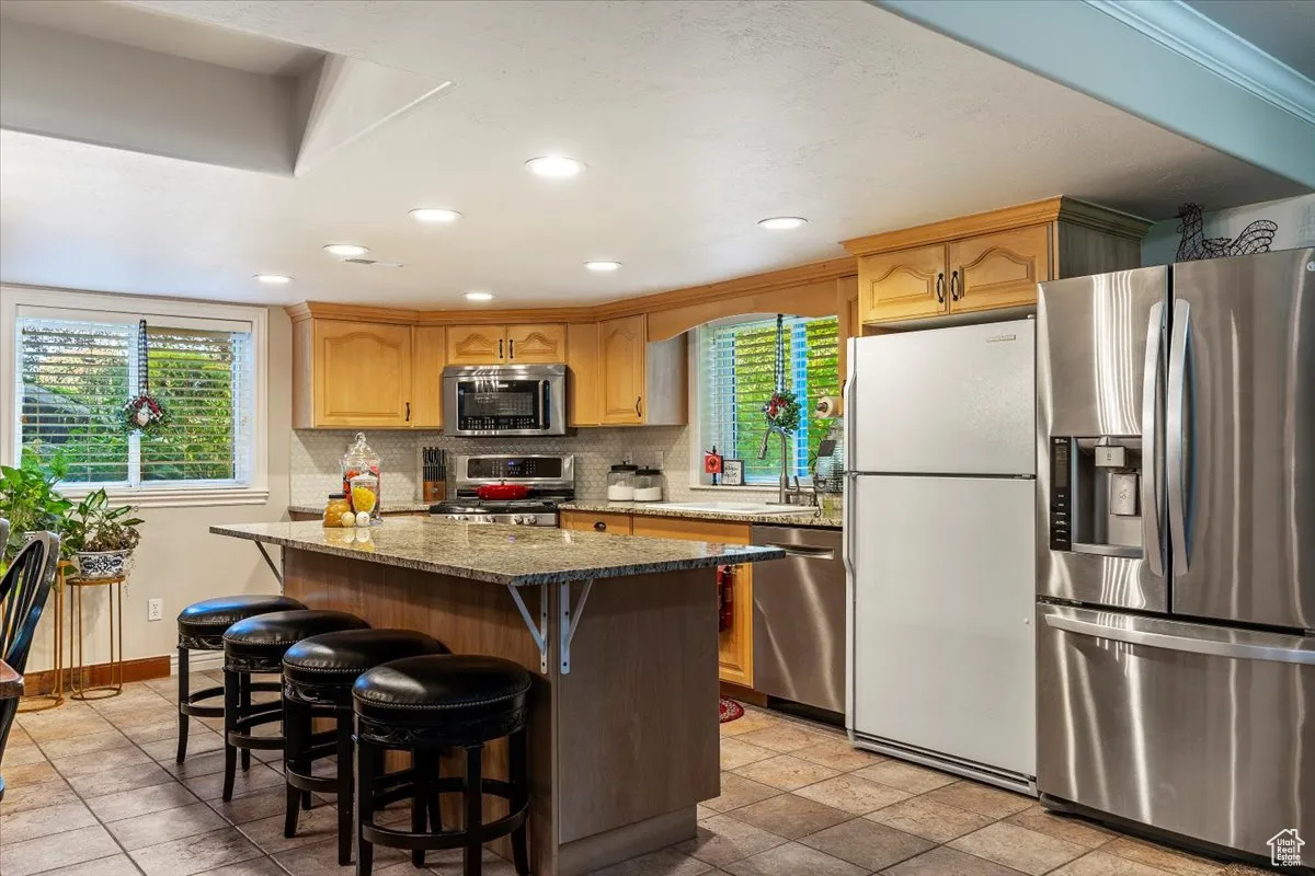 Kitchen featuring appliances with stainless steel finishes, dark stone counters, a breakfast bar area, a center island, and recessed lighting