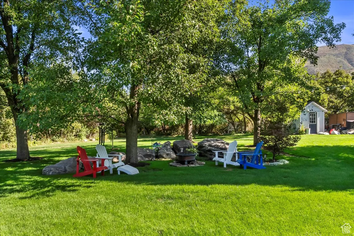View of green lawn featuring a fire pit, view of scattered trees, and an outbuilding