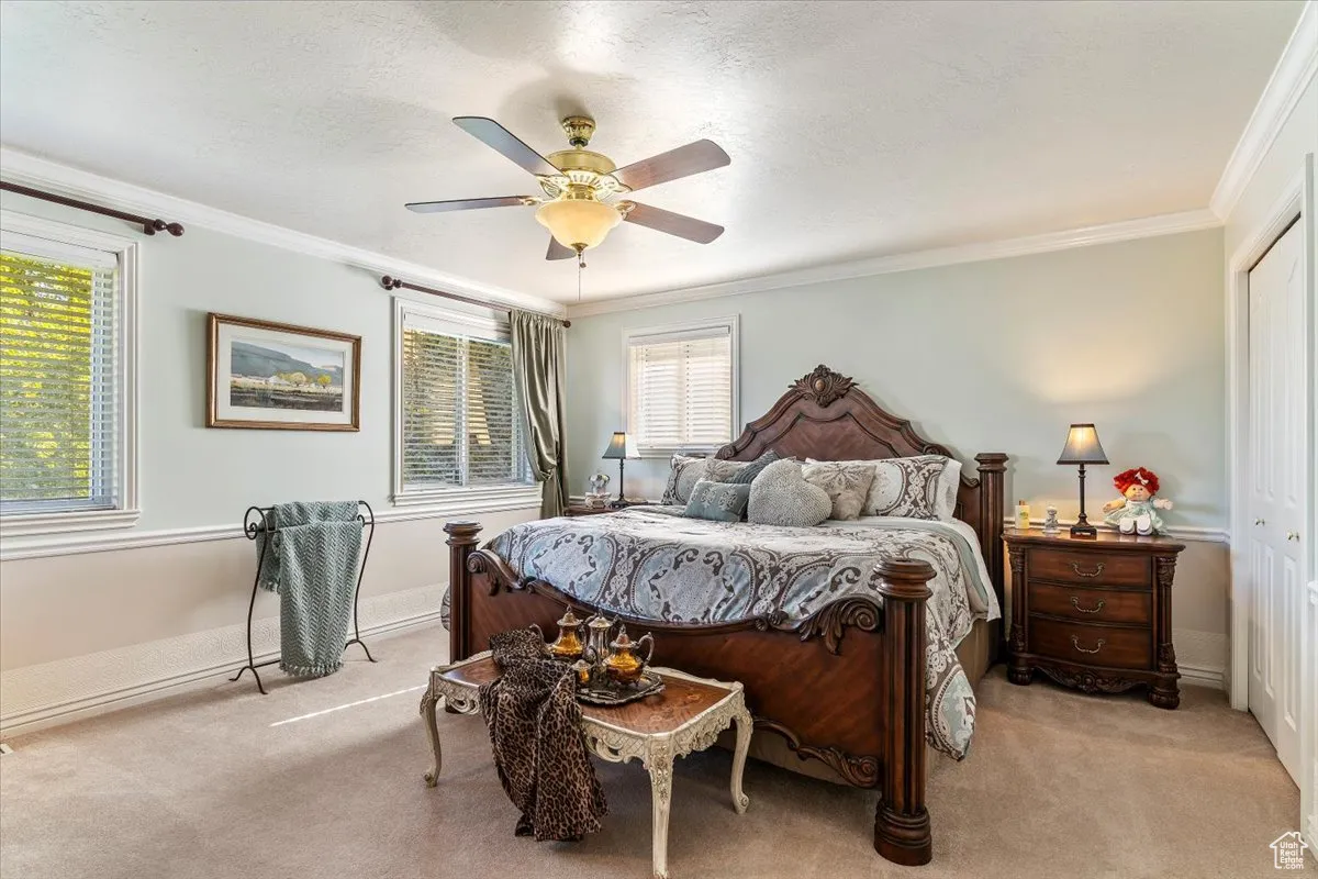 Bedroom featuring carpet, multiple windows, a textured ceiling, crown molding, and ceiling fan