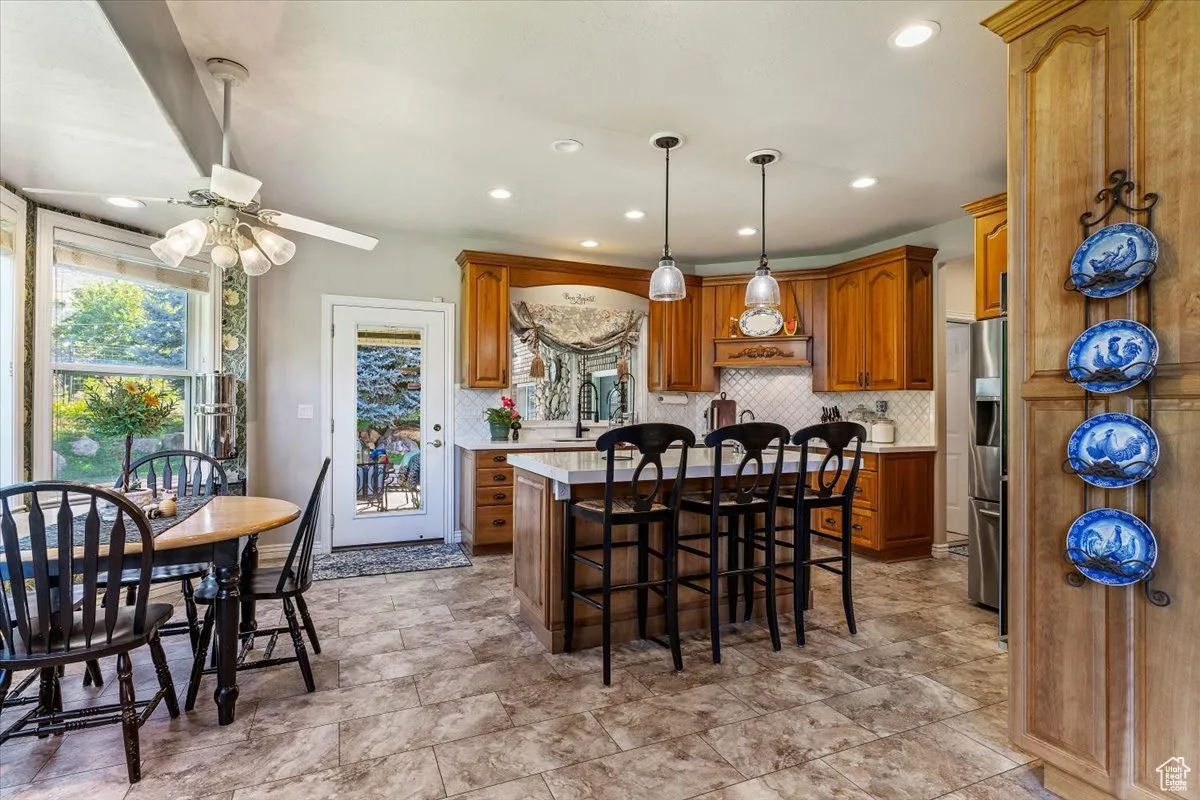 Kitchen featuring a breakfast bar, backsplash, brown cabinets, pendant lighting, and a kitchen island