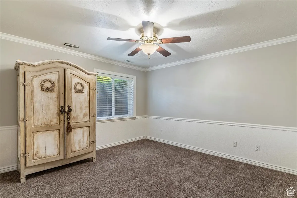 Unfurnished bedroom with crown molding, a textured ceiling, dark carpet, and ceiling fan