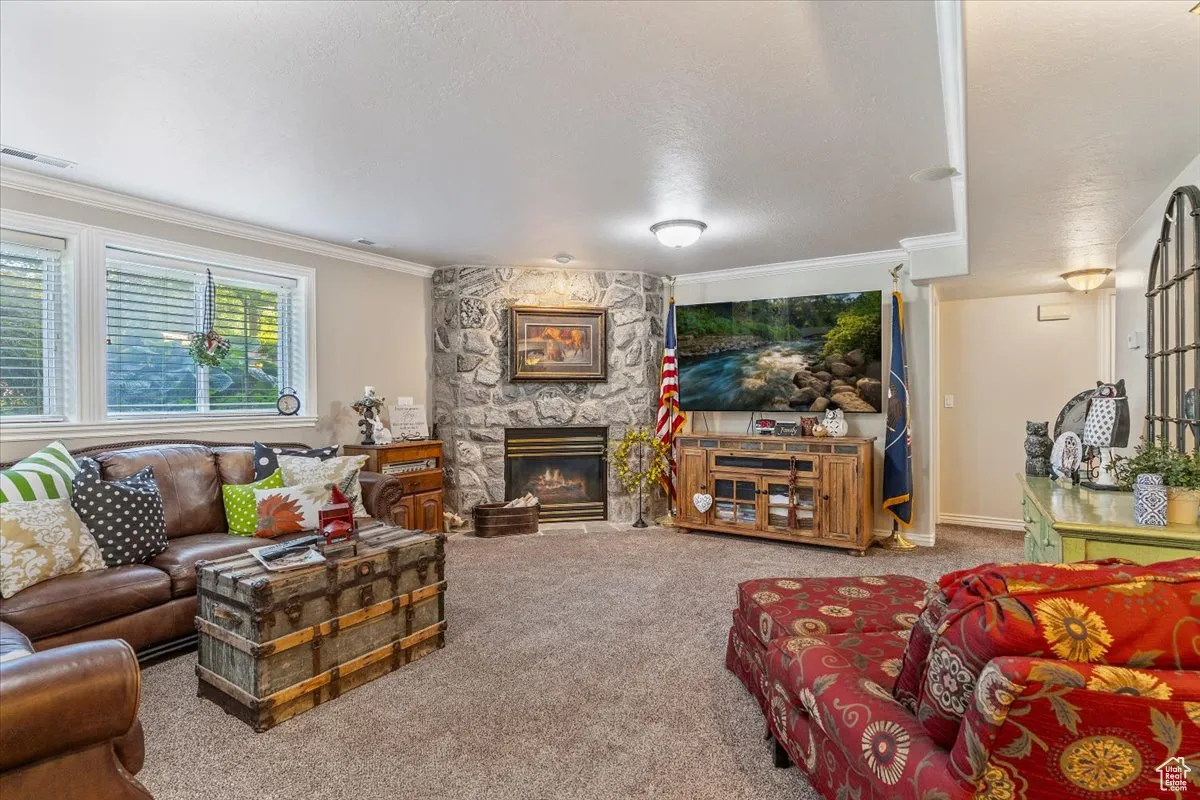 Living room featuring ornamental molding, a fireplace, carpet flooring, and a textured ceiling