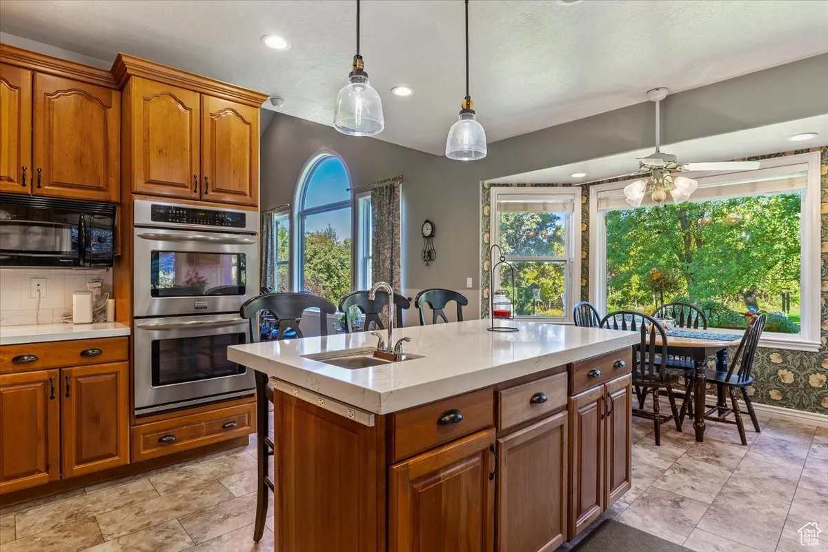 Kitchen with brown cabinetry, stainless steel double oven, black microwave, hanging light fixtures, and recessed lighting