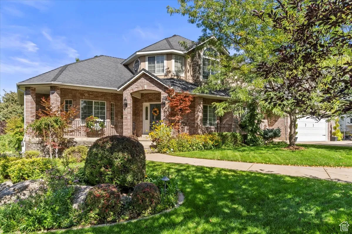 Traditional-style home featuring a porch, brick siding, a front lawn, and a shingled roof