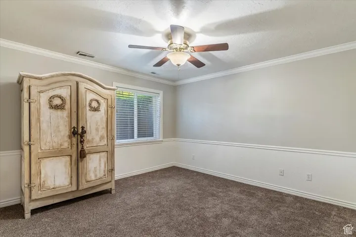 Unfurnished bedroom with crown molding, a textured ceiling, dark carpet, and ceiling fan