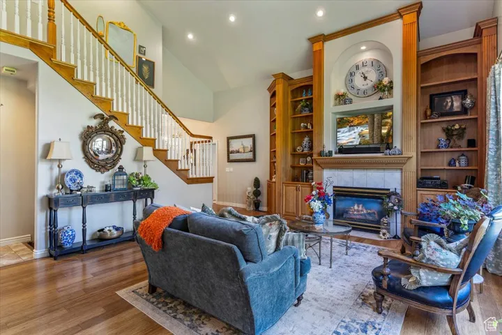 Living room with recessed lighting, a tile fireplace, built in features, wood finished floors, and high vaulted ceiling