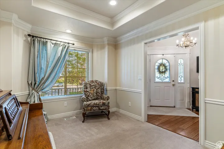 Foyer with a raised ceiling, light colored carpet, a chandelier, ornamental molding, and recessed lighting