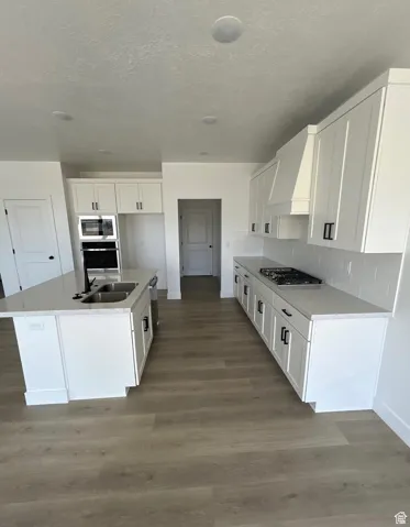 Kitchen featuring an island with sink, light wood-type flooring, white cabinetry, light stone counters, and a textured ceiling