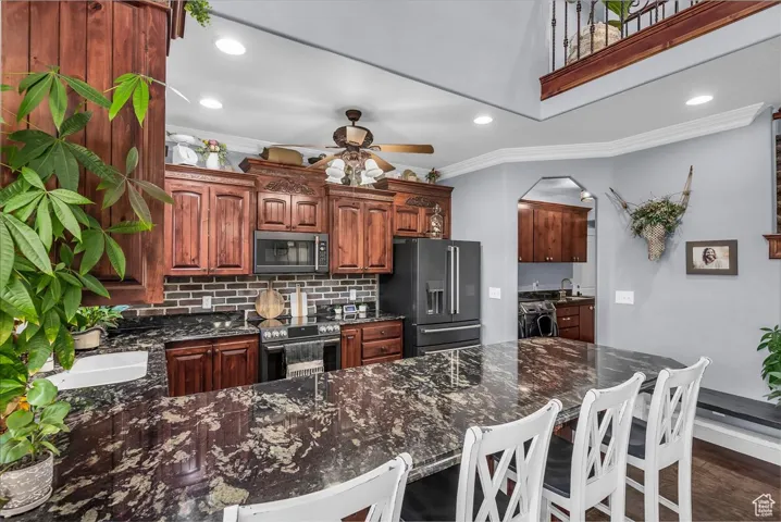 Kitchen with dark stone counters, decorative backsplash, ornamental molding, a peninsula, and appliances with stainless steel finishes