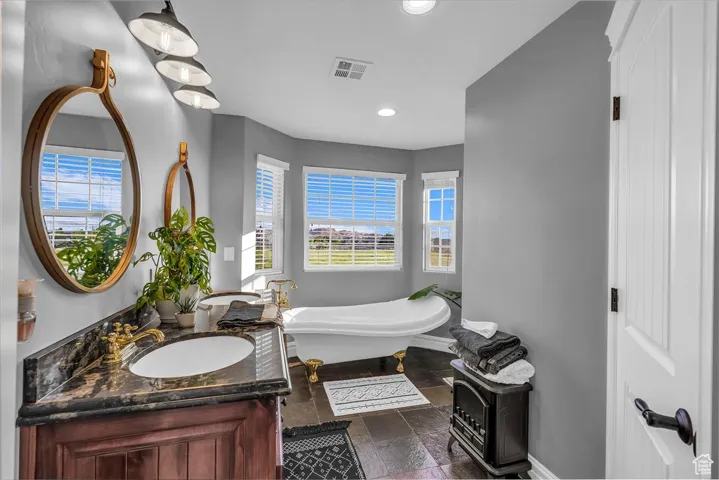 Full bathroom featuring a freestanding tub, double vanity, recessed lighting, and stone tile flooring