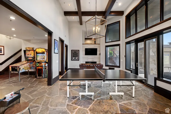 Game room featuring stone flooring, beamed ceiling, a high ceiling, recessed lighting, and a chandelier