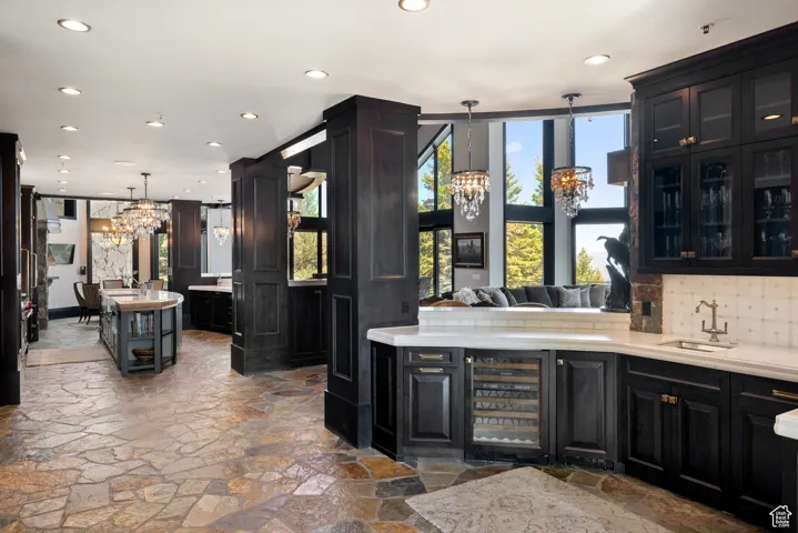 Bar with a chandelier, recessed lighting, beverage cooler, dark cabinets, and decorative light fixtures