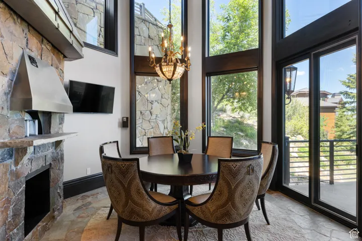 Dining room featuring a chandelier, healthy amount of natural light, a fireplace, and stone tile flooring