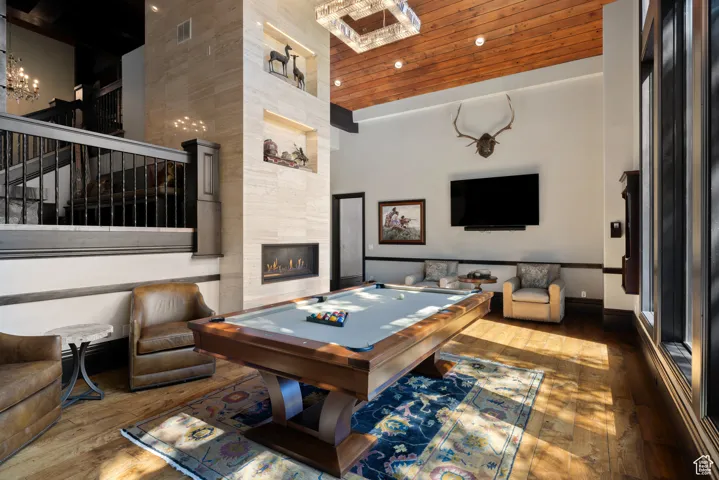 Game room featuring hardwood / wood-style floors, billiards table, a high ceiling, a fireplace, and a chandelier