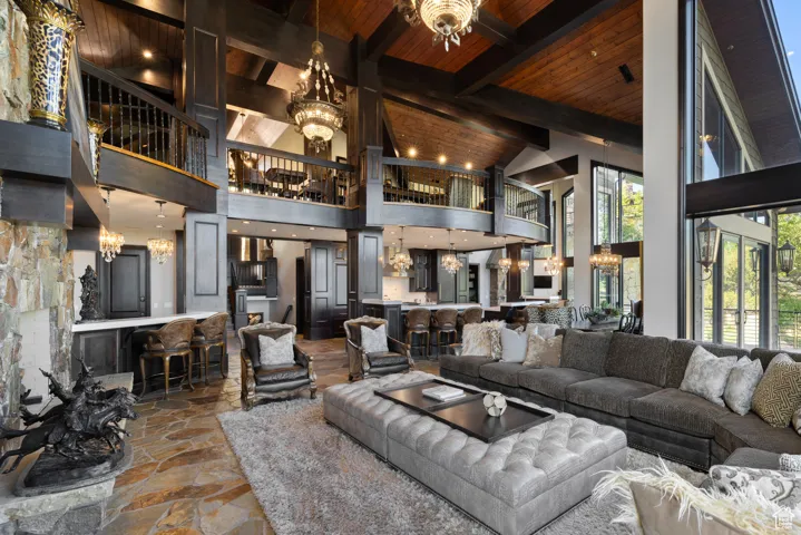 Living room with a chandelier, stone tile flooring, high vaulted ceiling, and a wooden ceiling with exposed beams