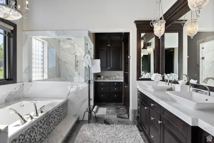 Bathroom with a chandelier, double vanity, a marble finish shower, a garden tub, and dark marble finish flooring