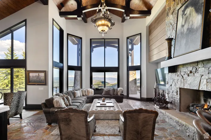 Living room featuring high vaulted ceiling, a stone fireplace, a chandelier, a wood ceiling with exposed beams, and healthy amount of natural light