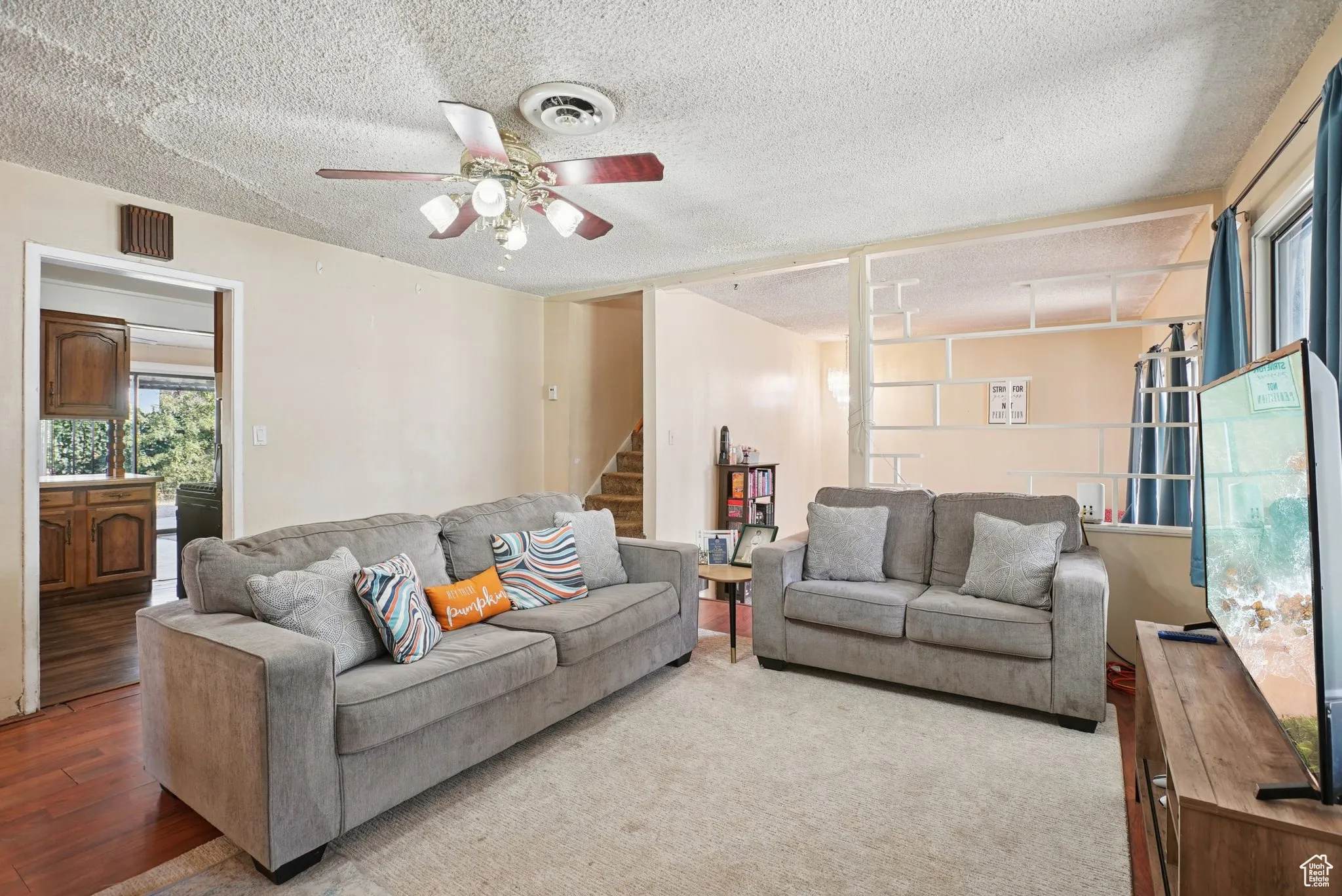 Living room with a textured ceiling, wood finished floors, stairs, and ceiling fan