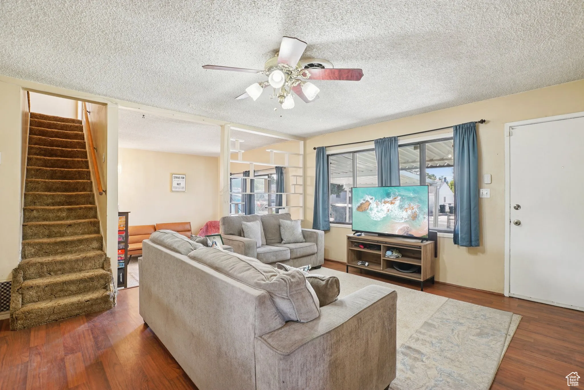 Living area featuring a textured ceiling, dark wood-type flooring, stairway, and ceiling fan
