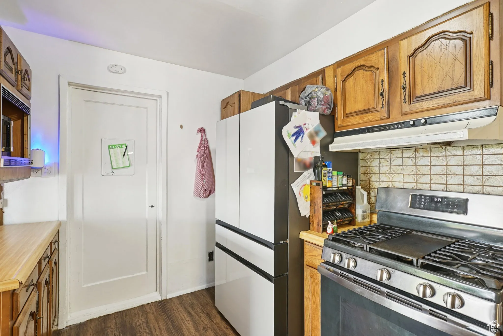 Kitchen featuring stainless steel range with gas cooktop, brown cabinets, decorative backsplash, light countertops, and dark wood-type flooring