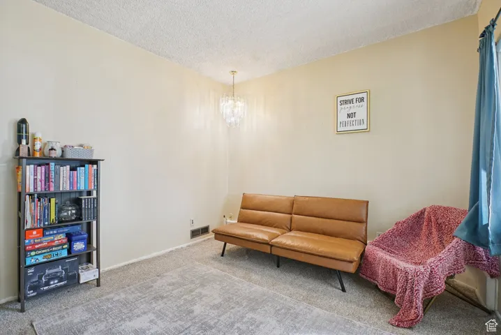 Living area with carpet flooring, a textured ceiling, and a chandelier