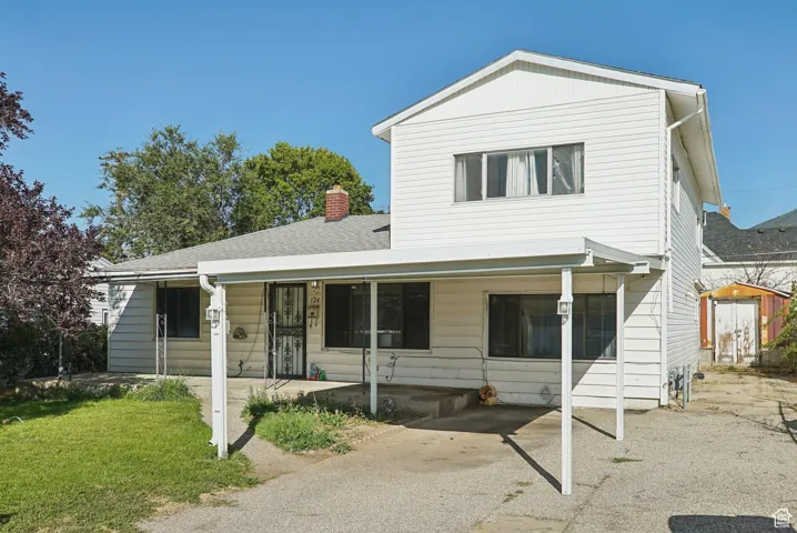 View of front of house featuring a storage shed, a chimney, and a shingled roof