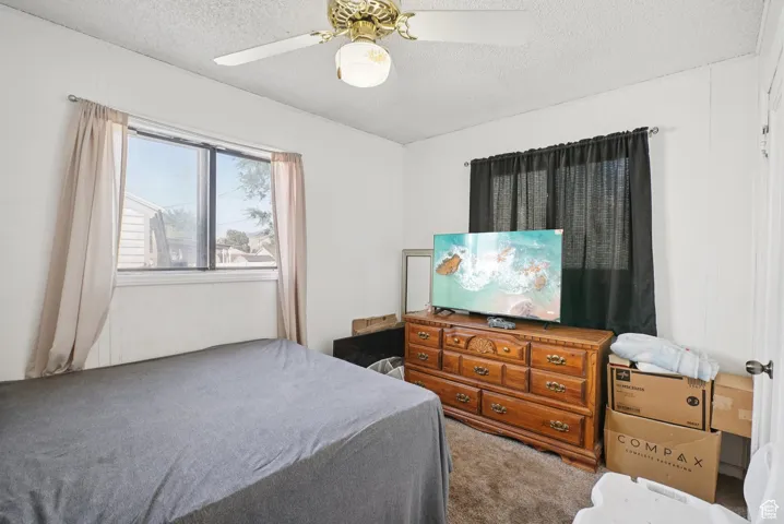 Bedroom with a textured ceiling, carpet flooring, and a ceiling fan