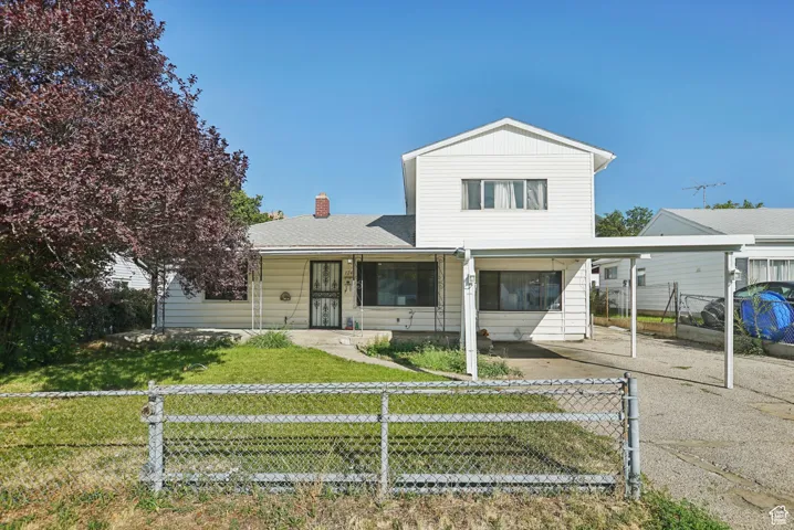View of front facade featuring a fenced front yard, a chimney, driveway, and an attached carport