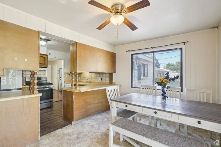 Kitchen with light countertops, decorative backsplash, stainless steel gas range oven, brown cabinets, and a peninsula
