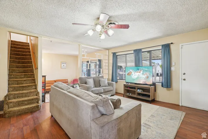 Living area featuring a textured ceiling, dark wood-type flooring, stairway, and ceiling fan