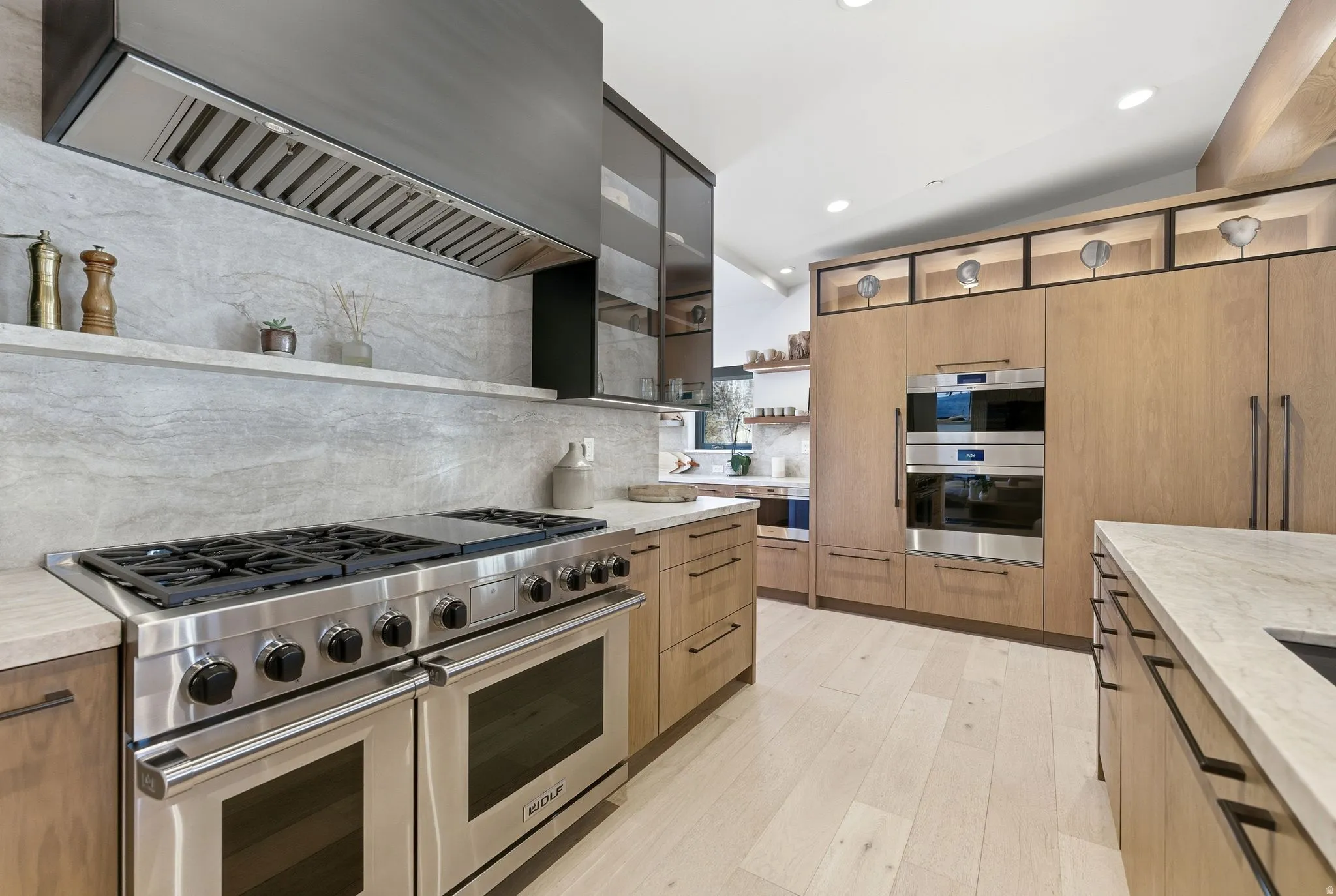 Kitchen with open shelves, premium range hood, appliances with stainless steel finishes, modern cabinets, and light stone counters