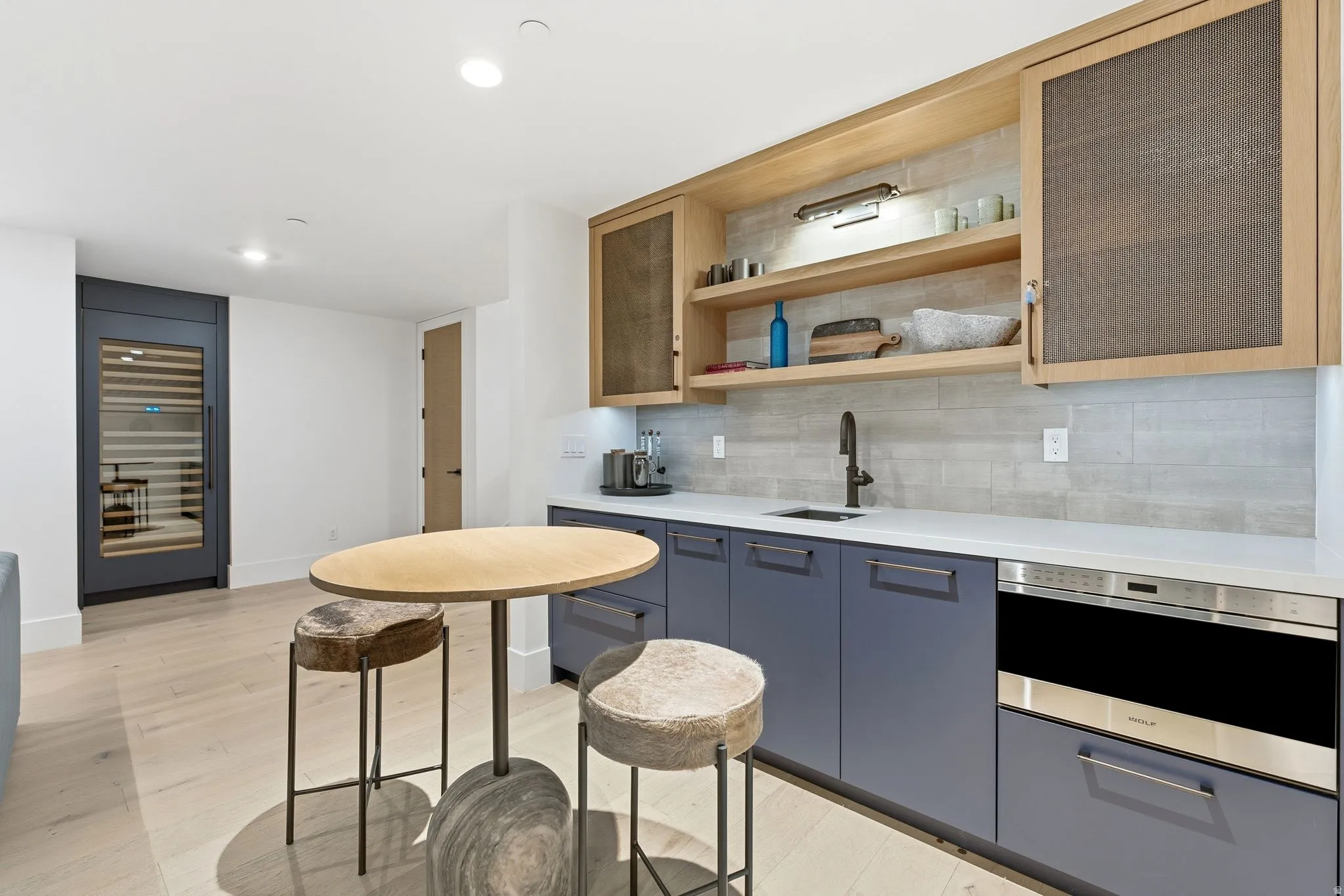 Kitchen with tasteful backsplash, open shelves, glass insert cabinets, light stone counters, and recessed lighting