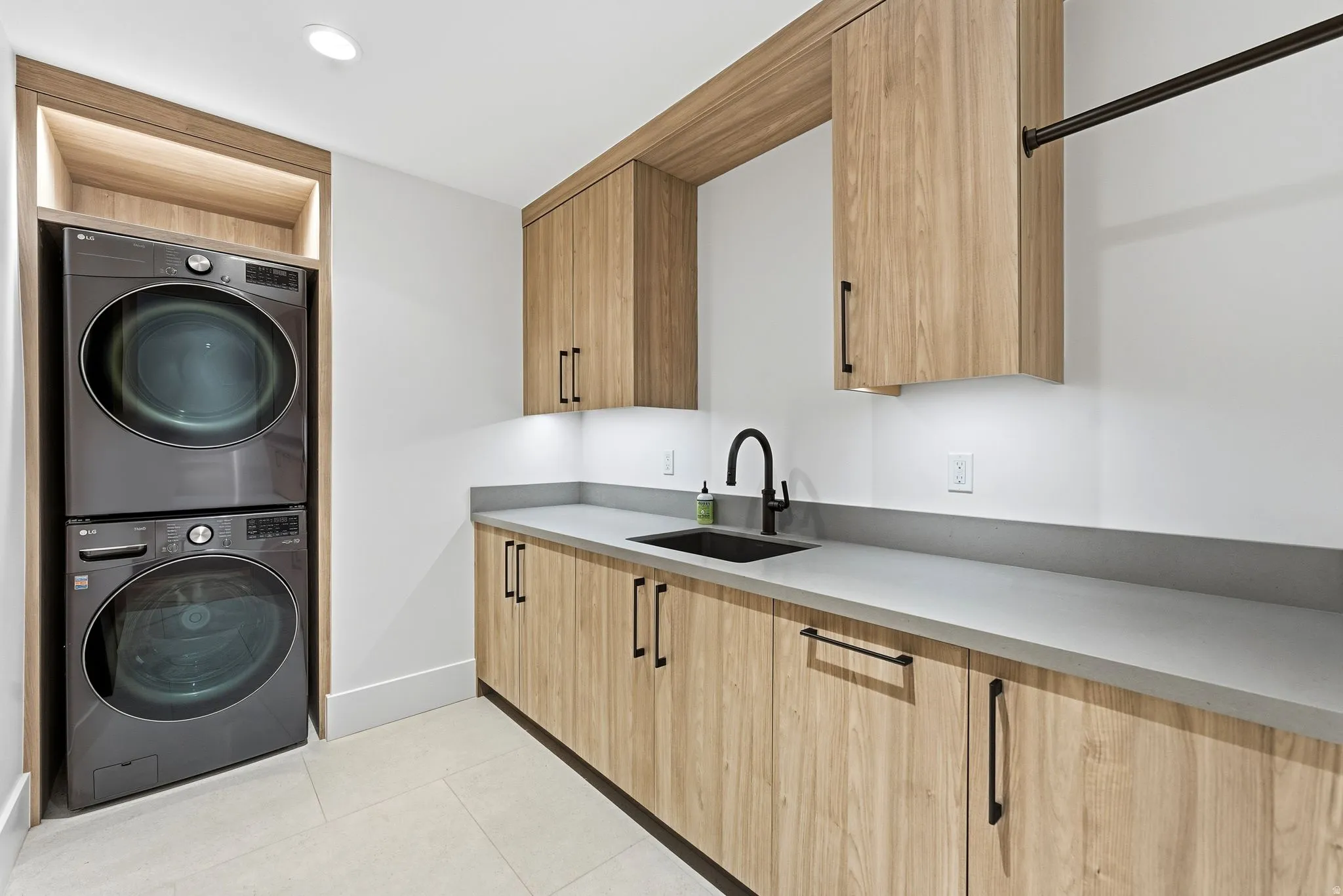 Laundry room with estacked washer and dryer, light tile patterned flooring, and recessed lighting